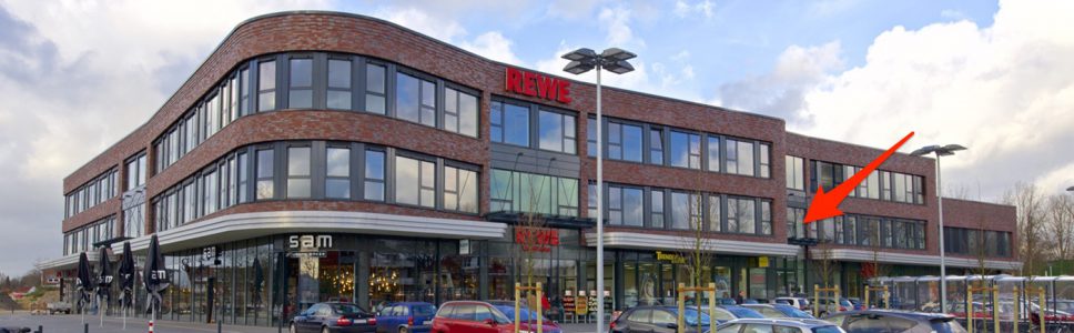 Gebäudeansicht mit REWE, Pfeil markiert die Lage der Kanzlei im Obergeschoss